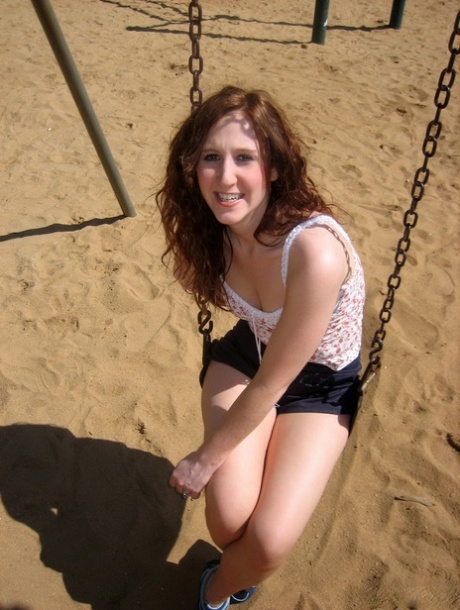 Redheaded girl crosses her legs while taking a swing at a public park 19804313